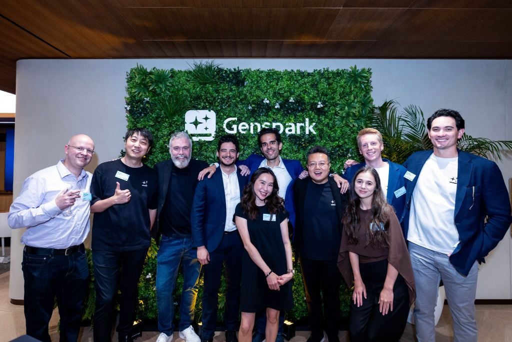 The Genspark team standing together in front of a Genspark living-wall logo